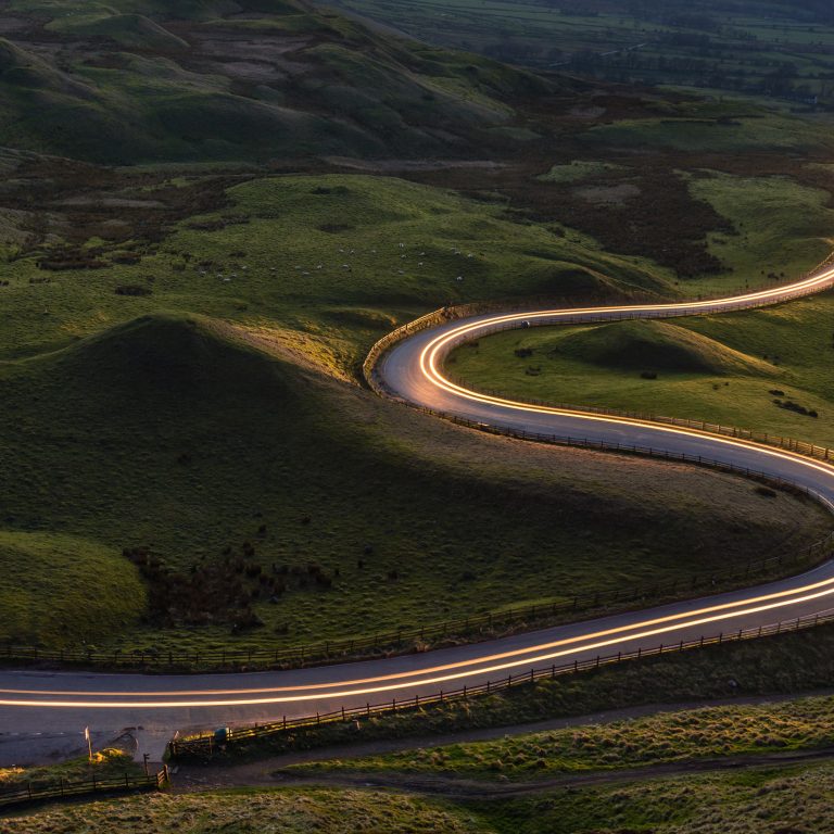 Winding curvy rural road with light trail from headlights leading through British countryside.