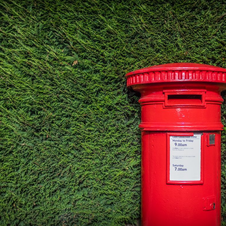 Red British post box set against a hedgerow