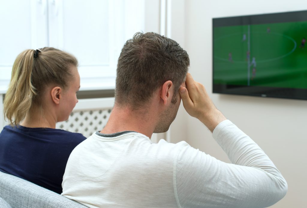 Sad couple watching football match on television at home.