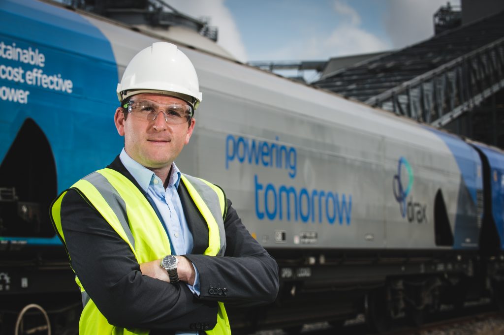 Drax Power CEO Andy Koss in a hard hat standing in front of a Drax biomass train