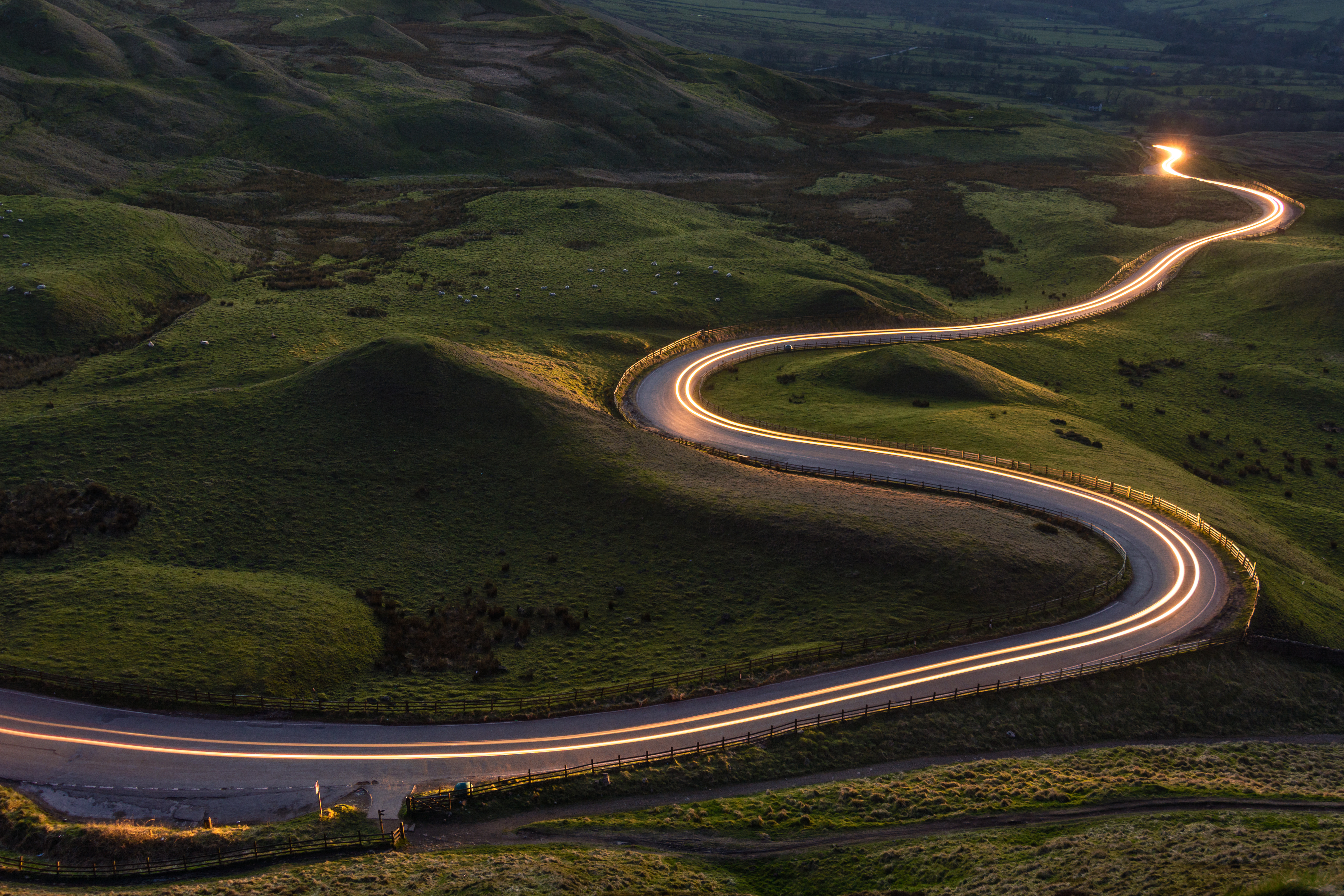 Winding curvy rural road with light trail from headlights leading through British countryside.