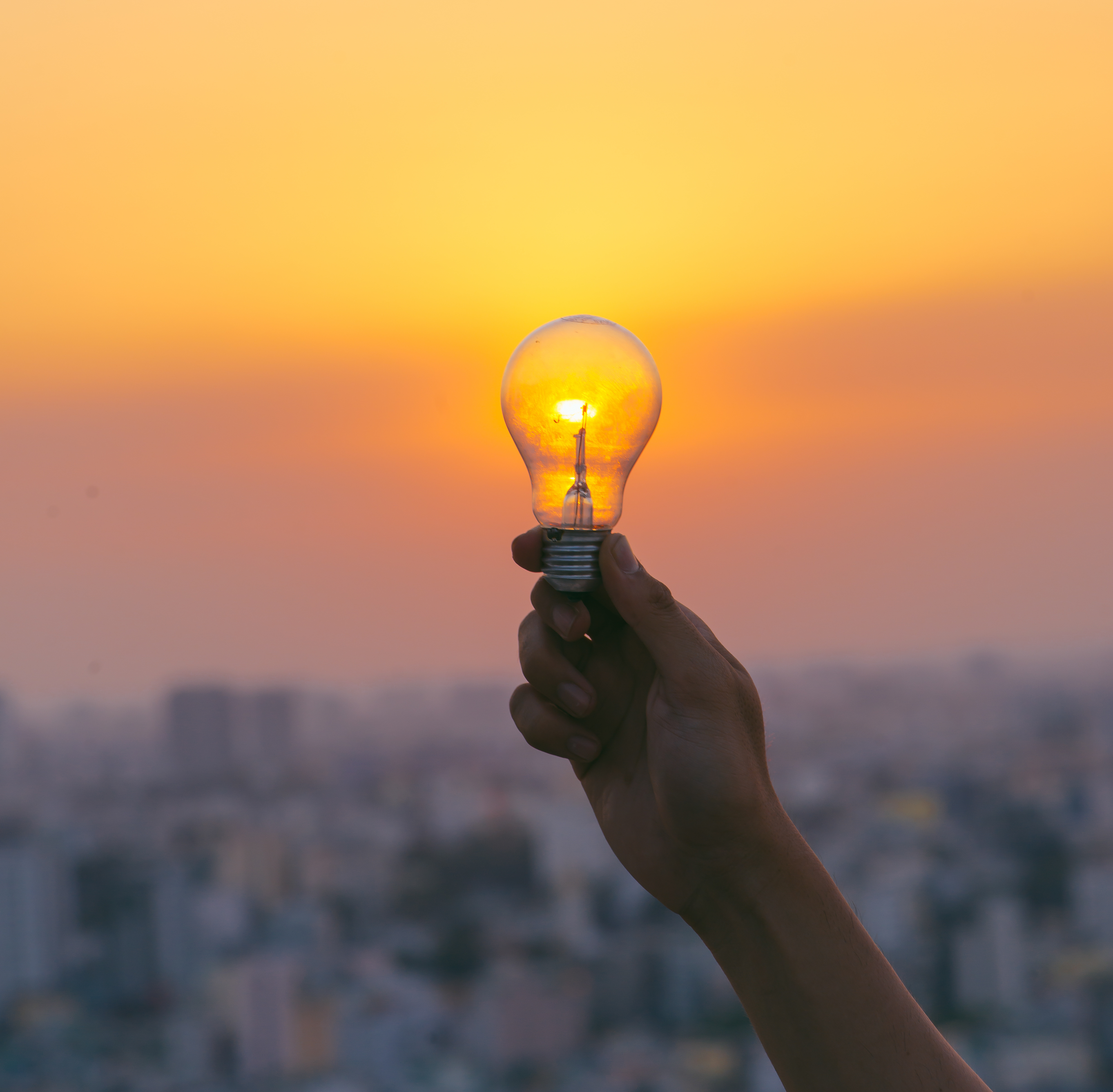 Hand hold a light bulb on sunset background for saving energy and creative concept.