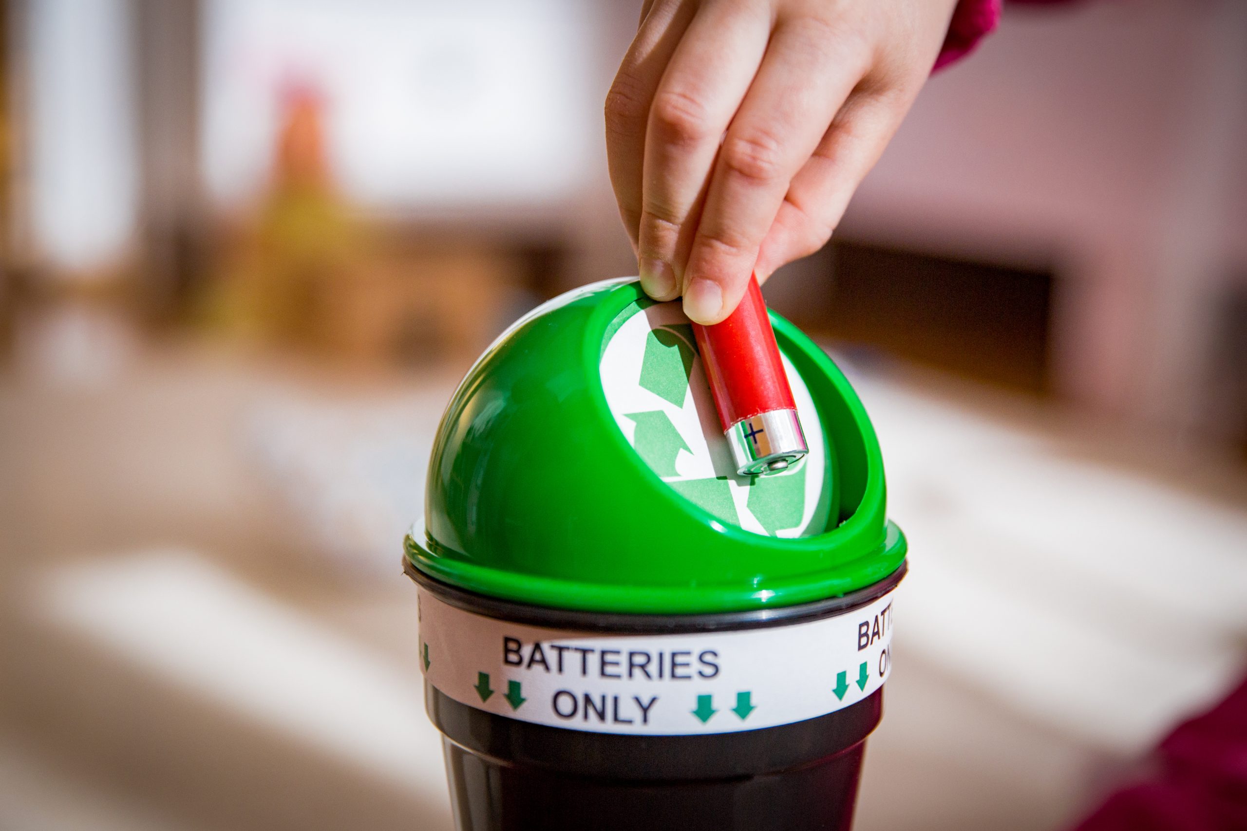 Little girl putting used batteries into recycling box at home. Child in