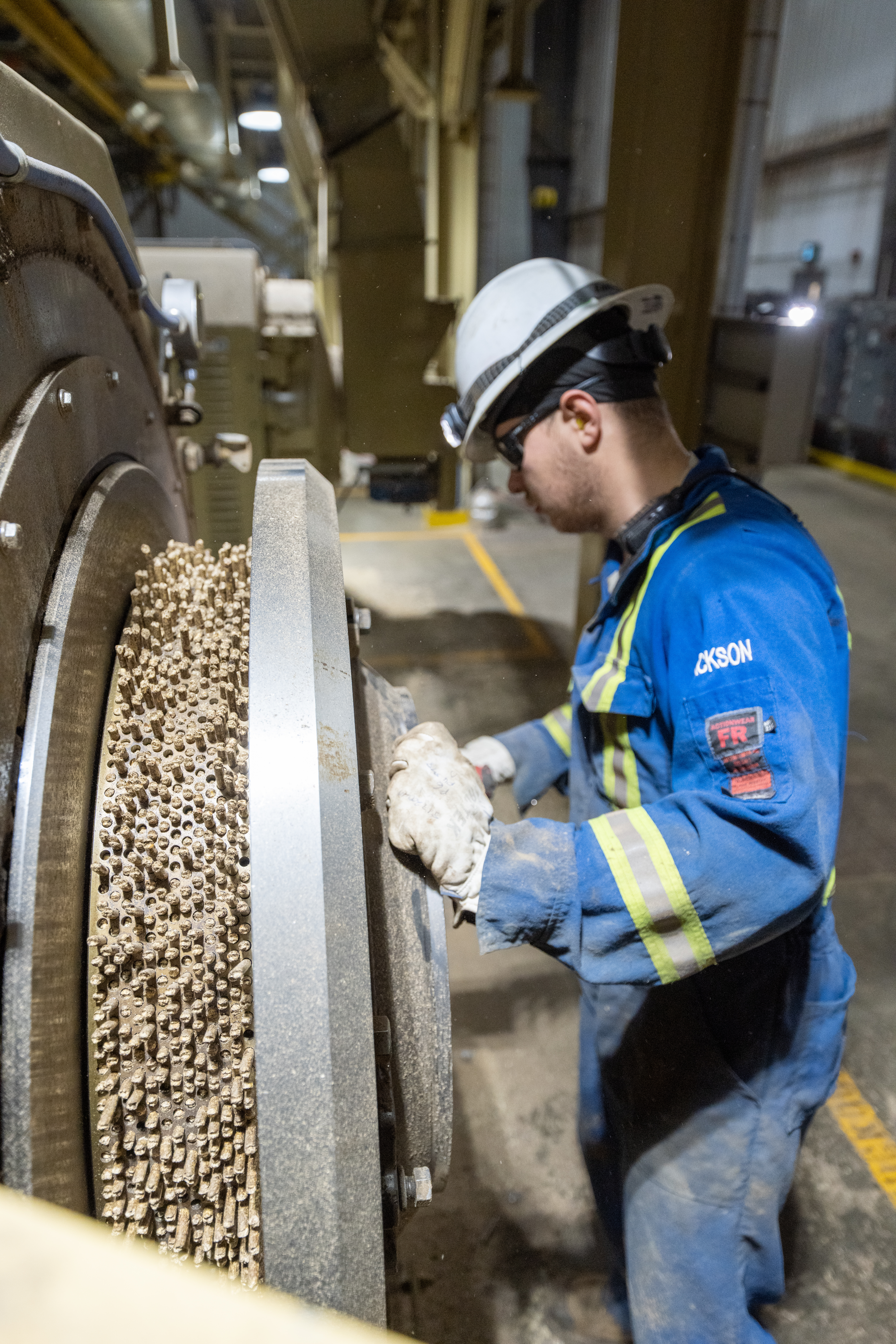 Worker in PPE operating machinery to create sustainable biomass pellets