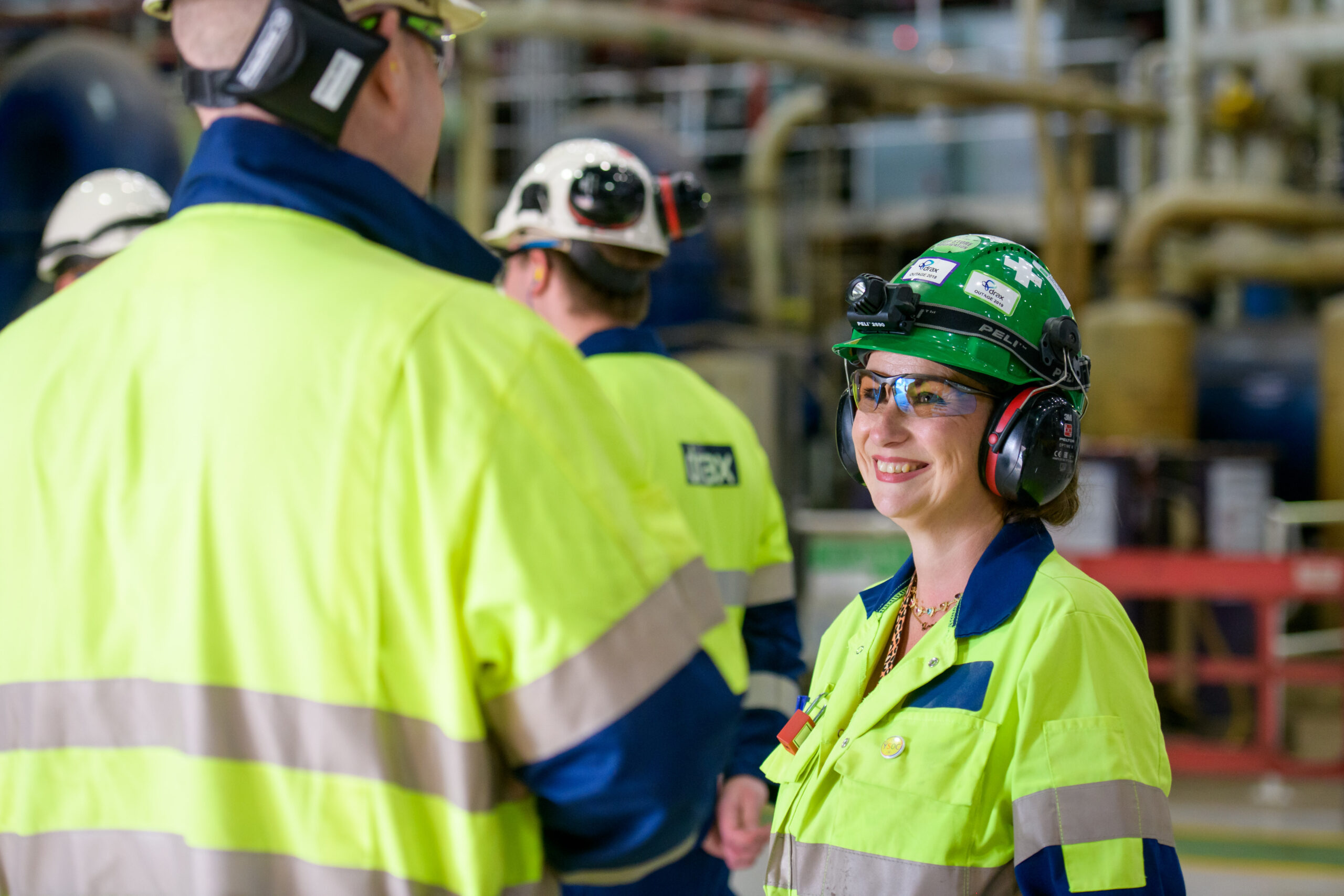 Workers in PPE smiling and talking in Drax Power Station turbine hall