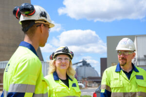 Drax workers in PPE speaking in front of biomass domes and cooling towers